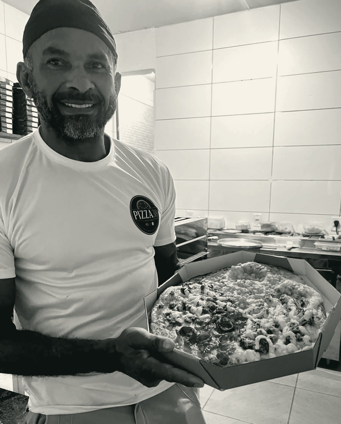 Xexeu Antunes, dono da Pizza 38, na cozinha, segurando uma pizza de quatro sabores na caixa