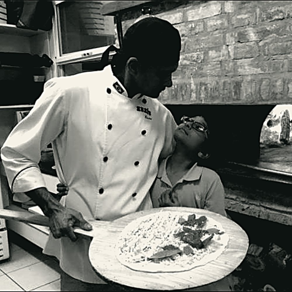 Xexeu com uma criança ao lado, segurando a pá com uma pizza pronta para enfornar