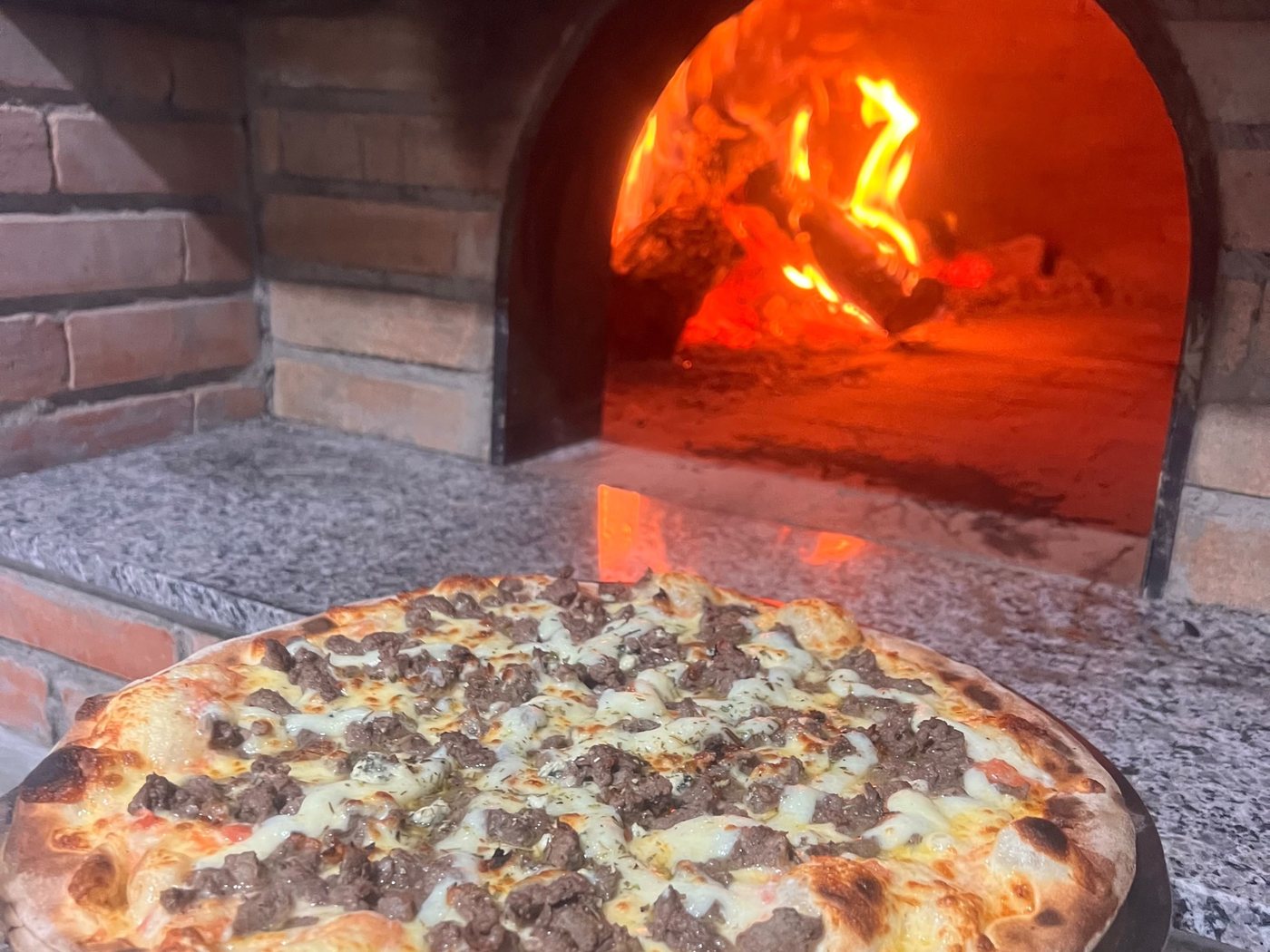 O forno a lenha da casa, de tijolo, com a lenha acesa ao fundo