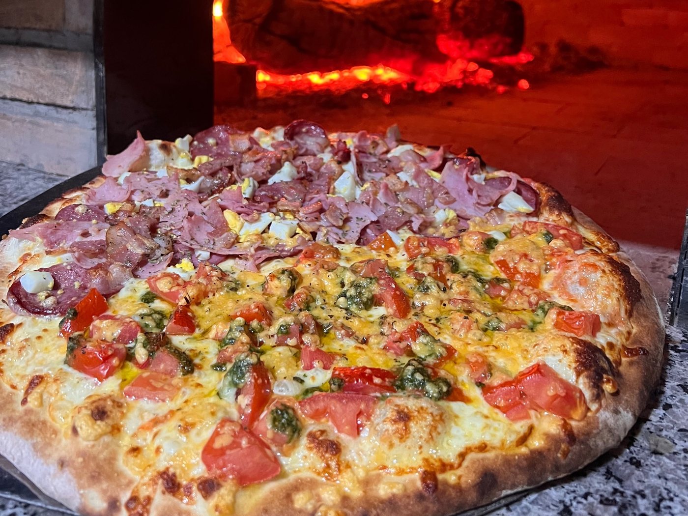 Pizza meia presunto meia pesto saindo do forno